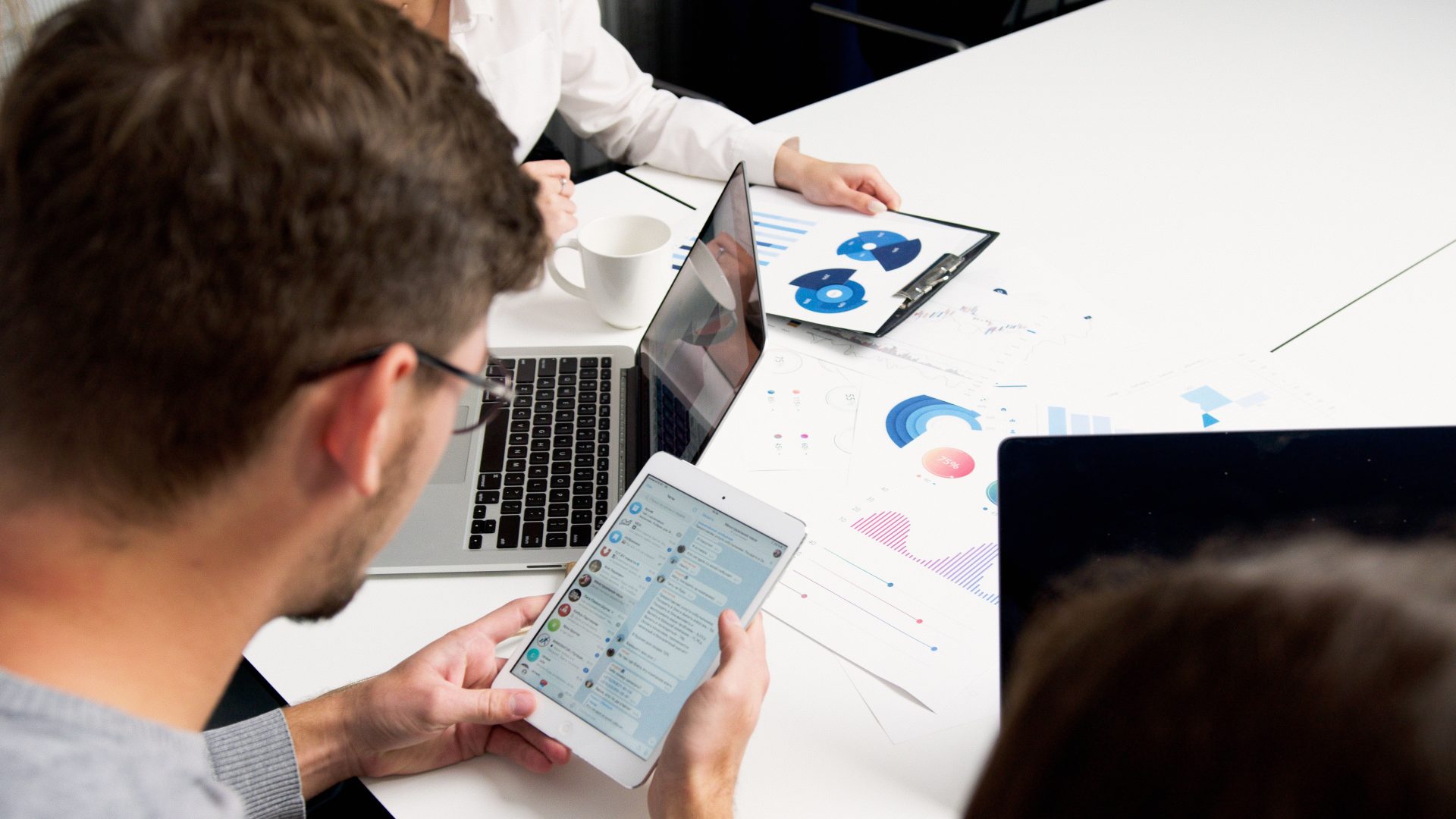 Moderne Team-Zusammenarbeit im Büro mit Laptops und Tablets, wobei der Fokus auf Diagrammen und Kommunikation liegt.